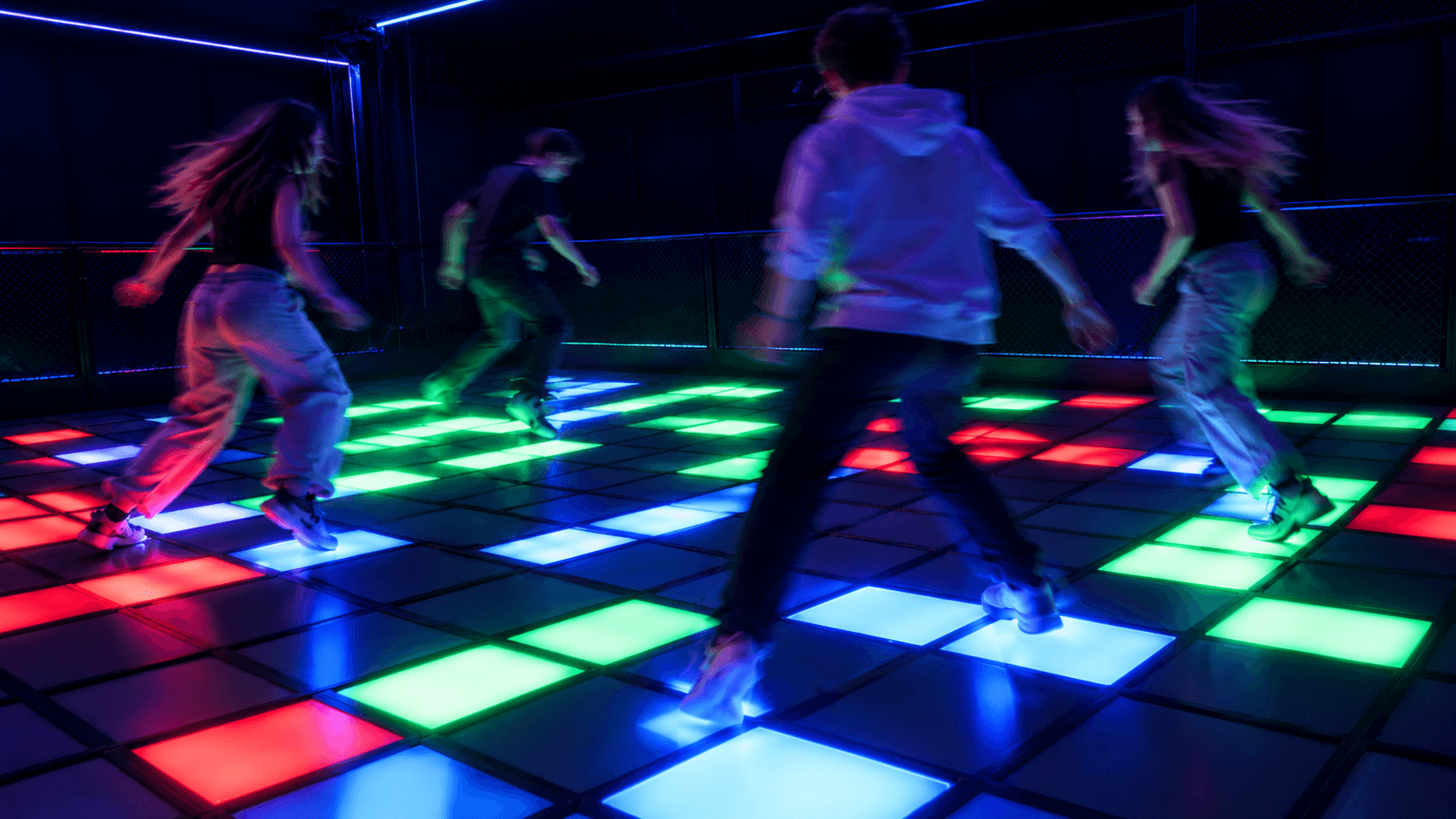 Four people playing an interactive pixel gaming floor, with illuminated red, green, blue and white floor tiles creating a dynamic game environment.